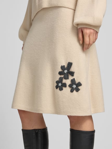 Frauenmodel trägt Knielanger Strickrock mit Stitchings und Perlen von Christian Berg Woman aus reiner Wolle, A-Linie, Nahaufnahme Oberkörper.