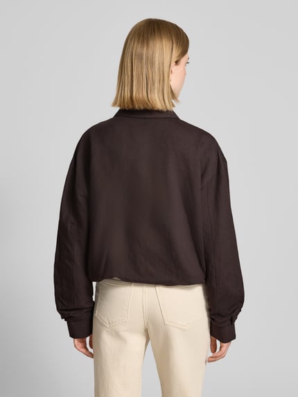 Frauenmodel trägt Jacke mit Umlegekragen Modell 'Nisari' von Someday aus reiner Baumwolle in Dunkelbraun, strukturierte Oberfläche, Regular Fit, Knopfleiste und Tunnelzug, kombiniert mit heller Hose, Ganzkörperansicht Rückansicht.