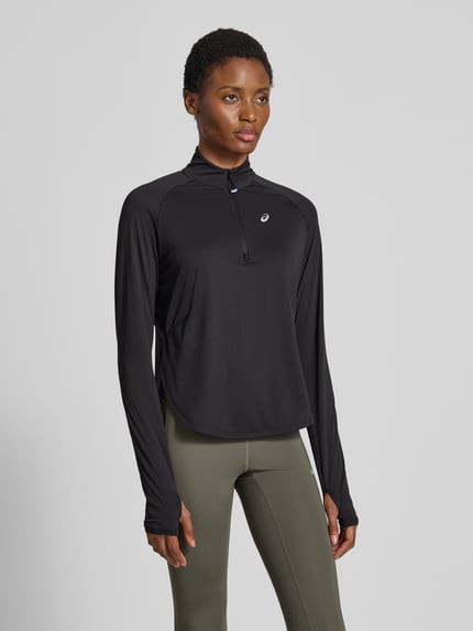 Frauenmodel trägt Longsleeve mit Troyer-Kragen Modell 'NAGINO' von ASICS TIGER in Schwarz, reflektierendes Logo, Raglanärmel, Ganzkörperansicht von vorne.