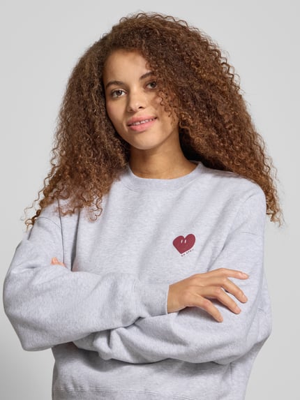 Frauenmodel trägt Sweatshirt mit Motiv-Print Modell 'Nina' von OH APRIL in Hellgrau aus Baumwoll-Mix, Relaxed-Fit, Nahaufnahme Oberkörper.