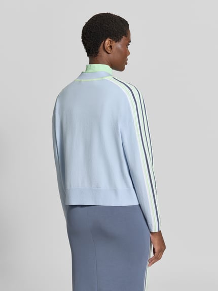 Frauenmodel trägt Strickjacke aus Lyocell-Mix mit Knopfleiste von Marc Cain, lockere Passform, Kontraststreifen, Ganzkörperansicht Rückansicht.