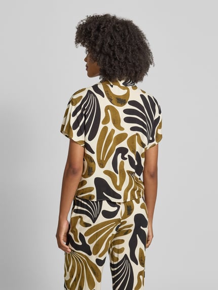 Vrouwenmodel draagt Regular Fit blouse uit zuiver viscose met knoopdetail model 'FELDI' van Soyaconcept, all-over look, overhemdkraag, verborgen knoopsluiting, ruglengte maat S 54 cm, mouwlengte maat S 10 cm, abstract patroon in zwart, mosterdgeel en beige, textiel met gladde structuur, geheel lichaam achteraanzicht.