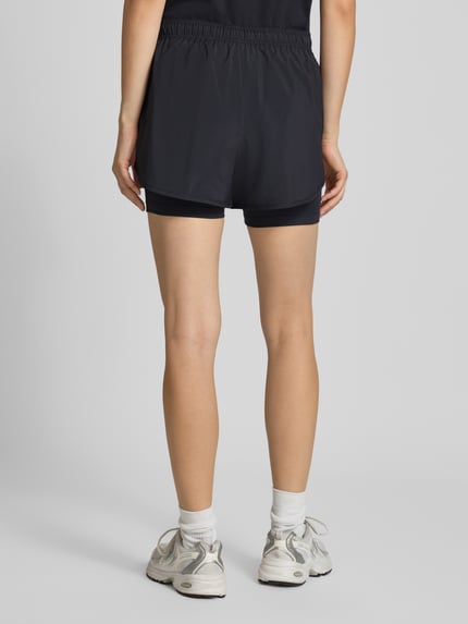 Frauenmodel trägt Shorts im 2-in-1-Look mit Logo von New Balance, elastischer Bund, schwarz, Regular Fit, Ganzkörperansicht Rückansicht.