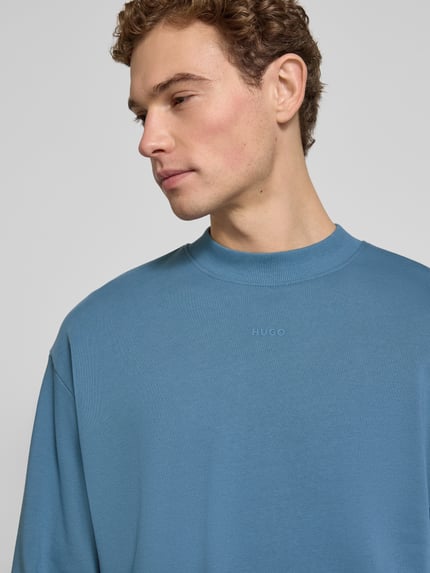 Männermodel trägt Regular Fit Sweatshirt aus reiner Baumwolle Modell 'DAPOCREW' von HUGO in Blau, Rundhals, Label Print, Nahaufnahme Oberkörper.