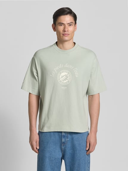 Männermodel trägt Relaxed Fit T-Shirt aus reiner Baumwolle Modell 'BOXYNORMAN GRAPHIC' von SELECTED HOMME, hellgrün, Motiv-Print, Rundhals, Kurzarm, Jersey-Textur, Ganzkörperansicht von vorne