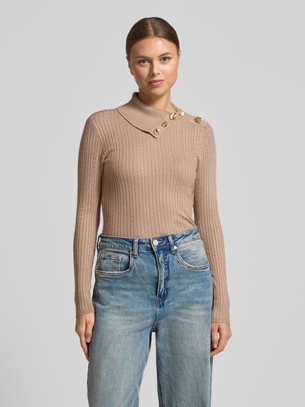 Modelka nosi Slim Fit Longsleeve aus Viskose-Mix Modell 'Sicilla' od Guess w kolorze beżowym, strick-optik, dekoracyjne guziki, krój slim fit, długi rękaw, długość tyłu w rozmiarze S: 52 cm, długość rękawa w rozmiarze S: 61 cm, widok całej sylwetki z przodu.
