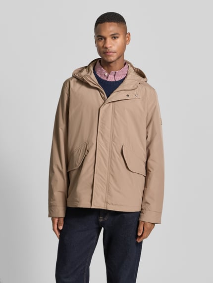Männermodel trägt Regular Fit Funktionsjacke mit Kapuze von Tommy Hilfiger in Optik: Unifarben, wasserabweisend, Ganzkörperansicht von vorne.