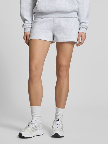 Frauenmodel trägt Regular Fit Sweatshorts mit Spitzenbesatz von Review, heller Material-Mix mit Baumwoll-Anteil, Ganzkörperansicht von vorne.