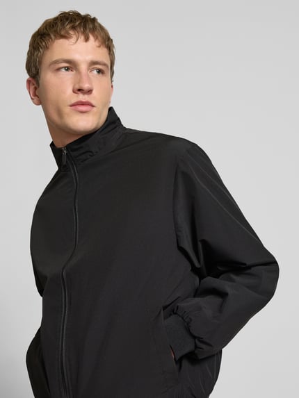 Männermodel trägt schwarze Regular-Fit Jacke mit Stehkragen Modell 'Charge' von JACK & JONES, Reißverschluss, Eingrifftaschen, elastische Abschlüsse, Nahaufnahme Oberkörper.