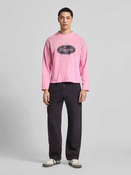 Męskimodel nosi różową bluzkę z długim rękawem z bawełny, krój relaxed fit, model 'Another Vintage' od ANOTHER COTTON LAB, z nadrukiem z logo i stójką, długość tyłu w rozmiarze M: 63 cm, widok całej sylwetki z przodu.