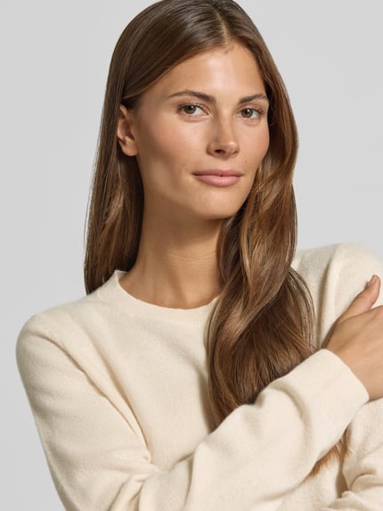 Frauenmodel trägt Slim Fit Strickpullover aus reinem Kaschmir von Christian Berg Woman in Creme, feine Textur, Nahaufnahme Oberkörper.