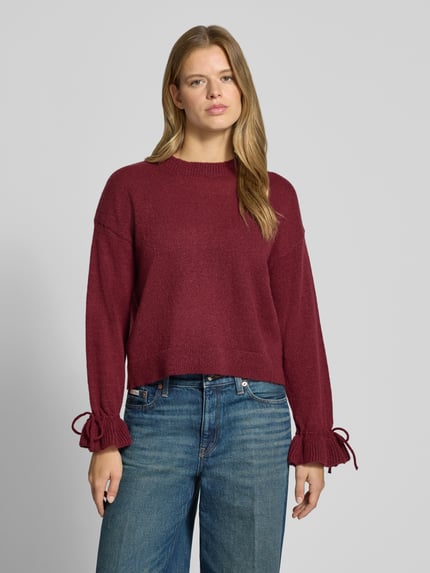 Frauenmodel trägt Pullover mit gerafften Ärmeln von PIECES in einfarbiger Strickoptik, Regular Fit, Longline, Rundhals, Nahaufnahme Oberkörper.