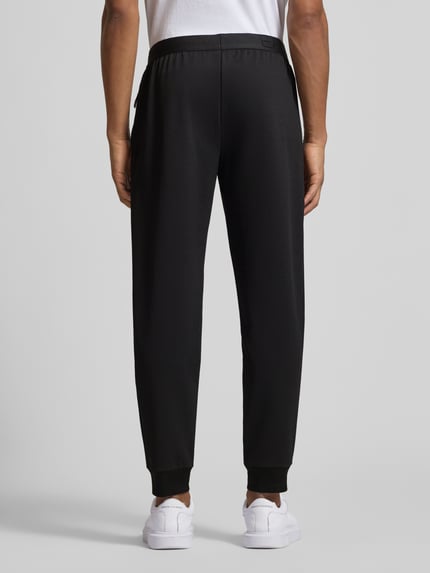 Männermodel trägt Sweatpants mit elastischem Bund und Label-Patch von EA7 Emporio Armani in Schwarz, lockere Passform, Ganzkörperansicht Rückansicht.
