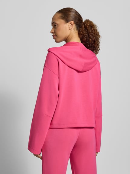 Frauenmodel trägt Regular Fit Sweatjacke mit Modal-Anteil von Christian Berg Woman in kräftigem Pink, strukturierte Oberfläche, Elastik-Material-Mix, Kapuze, Ganzkörperansicht Rückansicht, geteilter Känguru-Tasche und Tunnelzug.