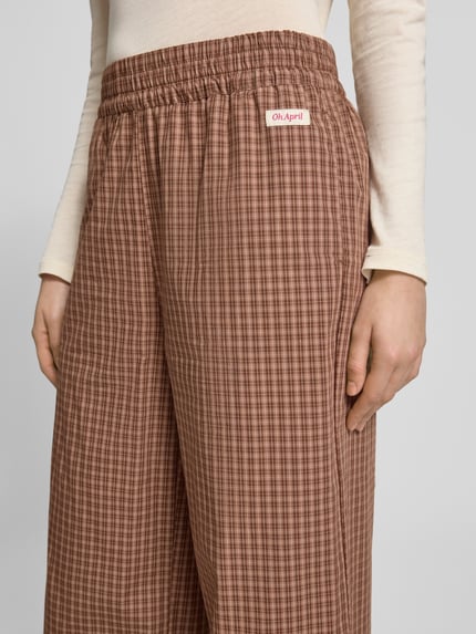 Männermodel trägt spodnie z szerokimi nogawkami Wide Leg Hose mit Label-Patch Model 'Hazel' von OH APRIL z bawełny, kratka, elastyczny pas, naszywka z logo, szerokość w rozmiarze S: 42 cm, długość wewnętrzna nogawki S: 79 cm, detailaufnahme okolicy pasa.