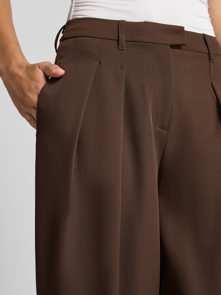 Frauenmodel trägt Barrel Fit Bundfaltenhose aus reiner Baumwolle Modell 'KIRSY' von ONLY, einfarbig braun, Webware, Nahaufnahme Oberkörper, seitliche Eingrifftaschen, Knopfverschluss, Gürtelschlaufen.