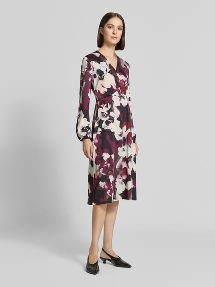 Frauenmodel trägt Midikleid in Wickel-Optik mit V-Ausschnitt von ZABAIONE, florales Muster mit A-Linie, Material-Mix, Ganzkörperansicht von vorne.