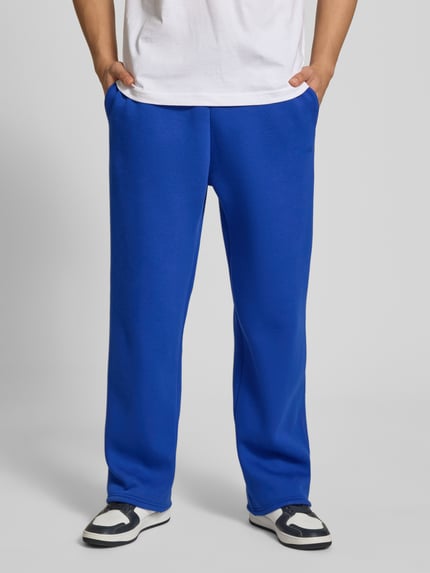 Męski model nosi Sweatpants mit elastischem Bund od REVIEW, mieszanka bawełny, krój relaxed fit, kieszeń z tyłu, długość wewnętrzna nogawki 76 cm, niebieskie, gładka tekstura, widok z przodu, zdjęcie całej sylwetki.