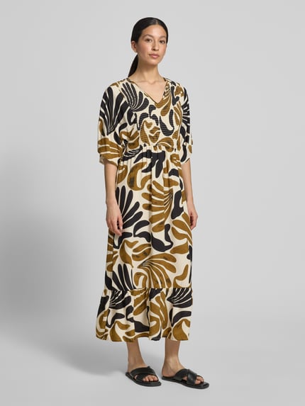 Vrouwenmodel draagt midi-jurk van zuiver viscose, getailleerd model met V-hals en smokdetail, model 'FELDI' van Soyaconcept, kleurenmix zwart, beige en wit, dames midi-jurk, ruglengte maat S: 119 cm, borstwijdte: 44 cm, mouwlengte: 25 cm, geheel van voren.