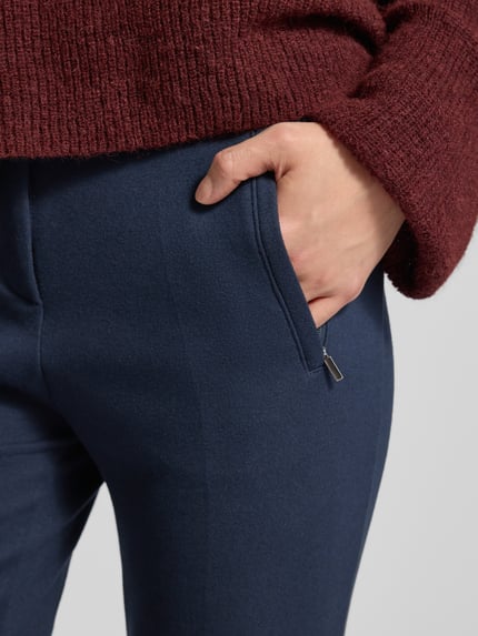 Kobieta nosi granatowe spodnie Stoffhose mit französischen Eingrifftaschen Modell 'Lillyth' od Raphaela By Brax, materiał z dodatkiem wiskozy, prosty krój, francuskie kieszenie, zbliżenie na kieszeń, ujęcie detaliczne.