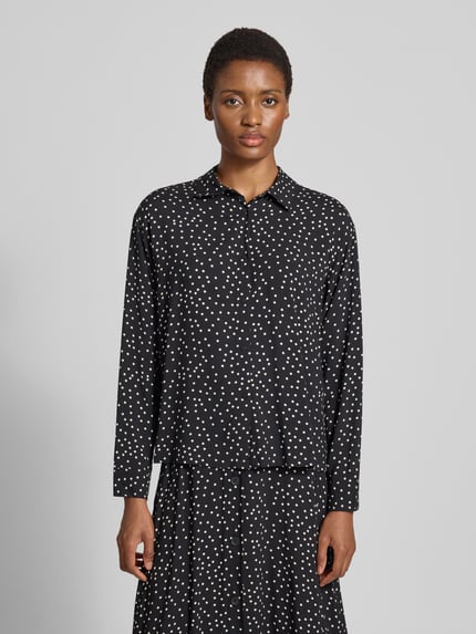 Frauenmodel trägt Regular Fit Hemdbluse aus reiner Viskose Modell 'GILDA' von Soyaconcept, schwarz mit weißen Punkten, Ganzkörperansicht von vorne, Kontext: Damen Hemdbluse, Hemdblusenkragen, langärmlig, durchgehende Knopfleiste, Rückenlänge 57 cm, Ärmellänge 57 cm.