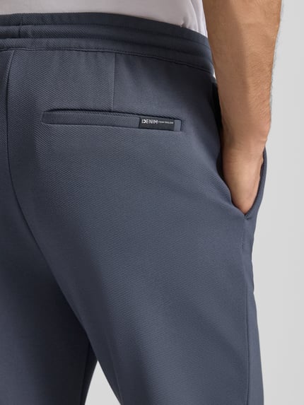 Męski model nosi Tapered Chino mit Viskose-Anteil od Tom Tailor Denim, kolor jednolity, tylne kieszenie, zbliżenie na biodra, detal.