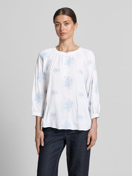 Frauenmodel trägt Bluse aus Viskose-Mix mit verlängertem Rücken von Apricot in Weiß mit hellblauem Muster, Loose-Fit, Rundhalsausschnitt, kurze Knopfleiste, Viskose-Baumwoll-Mix, Rückenlänge 68 cm, Ärmellänge 52 cm, Ganzkörperansicht von vorne.