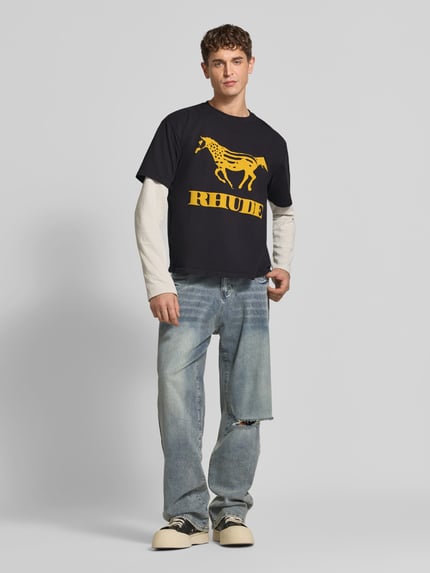 Männermodel trägt T-Shirt mit Label-Print von RHUDE aus reiner Baumwolle, gerader Schnitt, Rundhalsausschnitt, Dunkelblau mit gelbem Print, Ganzkörperansicht von vorne, Rückenlänge bei Größe M: 55 cm.