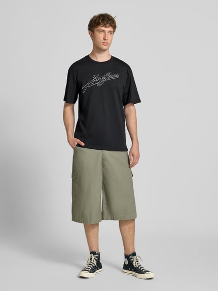 Männermodel trägt Oversized Fit T-Shirt mit Logo-Stitching von KARL KANI in Schwarz, Reine Baumwolle, Rundhalsausschnitt, Herren T-Shirt, Ganzkörperansicht von vorne, Rückenlänge bei Größe M: 72 cm.
