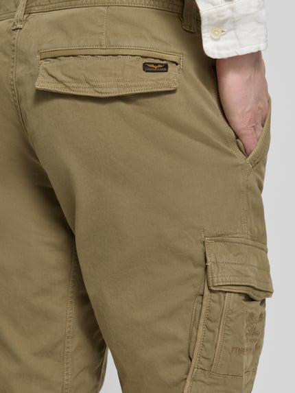 Männermodel trägt Bermudas mit Pattentaschen und Label-Stitchings von PME Legend in Khaki mit Motiv- und Label-Stitchings, Detailaufnahme Rückansicht. Bundweite 41 cm, Innenbeinlänge 26 cm, Seitliche Eingrifftaschen und Klettverschluss.