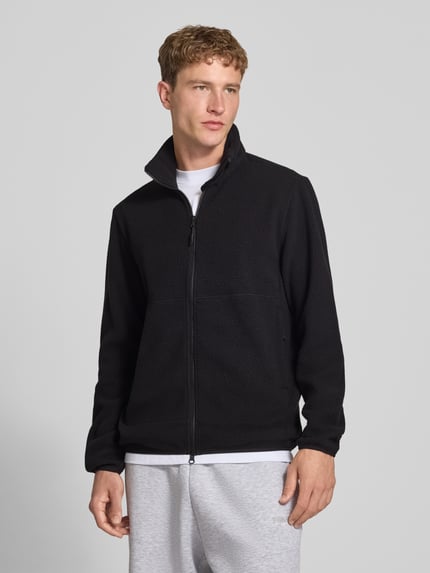 Mężczyzna nosi kurtkę z polaru w kolorze czarnym, model Regular Fit Fleecejacke mit Stehkragen Modell 'JASON' od ONLY & SONS, Ganzkörperansicht z przodu.