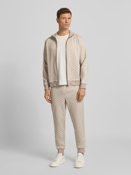Männermodel trägt Sweatpants mit elastischem Bund Modell 'Eliton' von JOOP! Collection im Material-Mix mit Viskose-Anteil, Lockerer-Schnitt, hellbeige Muster, französische Eingrifftaschen, Gesäßtasche und Tunnelzug, Ganzkörperansicht von vorne.