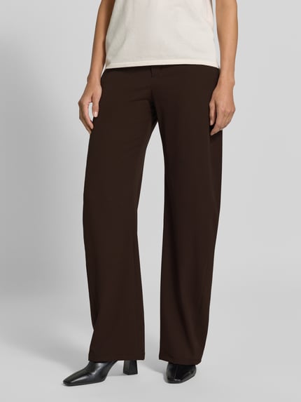 Frauenmodel trägt Barrel Fit Stoffhose mit Viskose-Anteil von DRYKORN in Dunkelbraun, lockerer Schnitt, glatte Textur, Nahaufnahme Unterkörper. Elastischer Material-Mix, Knopf- und Reißverschluss, Eingriff- und Leistentaschen.