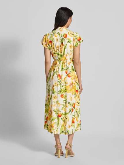 Frauenmodel trägt Abendkleid aus Leinen-Viskose-Mix Modell 'Posie' von Forever New mit gelb-grünem Muster und Taillenband, Ganzkörperansicht Rückansicht. Taillierte Passform, Stehkragen mit V-Ausschnitt, Kurzarm, Kontext: Rückenlänge Größe 36 ca. 38 cm, Brustweite 38 cm, Ärmellänge 16 cm.