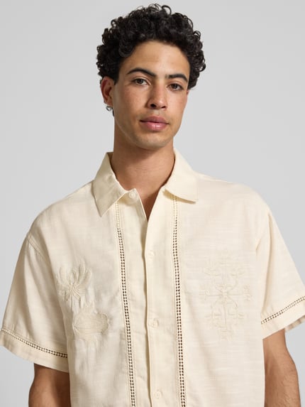 Mężczyznamodel nosi Relaxed Fit Freizeithemd aus Lyocell-Mix Modell 'Menton' od Jack & Jones, kremowy, haft kwiatowy, bawełna-lyocell, krój relaxed fit, krótki rękaw, kołnierz kent, pełna listwa guzikowa, szerokość w rozmiarze M: 52 cm, długość tyłu: 72 cm, długość rękawa: 25 cm, tekstura lekko fakturowana, widok z przodu, zbliżenie na górną część ciała.