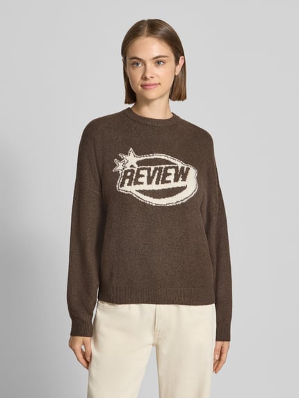 Frauenmodel trägt Strickpullover mit Label-Print von REVIEW in Braun, lässiger Schnitt, Rundhalsausschnitt, Ganzkörperansicht von vorne.