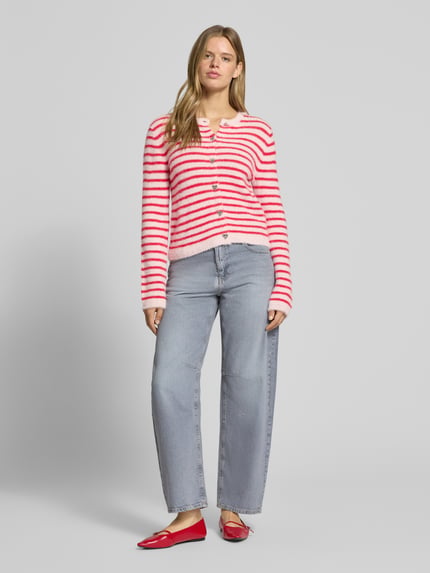 Frauenmodel trägt Strickjacke mit Herzknöpfen von ONLY in Rosa und Weiß mit Streifen, kombiniert mit Jeans, Ganzkörperansicht von vorne.