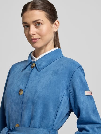 Frauenmodel trägt Trenchcoat mit Bindegürtel Modell 'CORDELIA' von Frieda & Freddies in Blau, Material-Mix mit Stretch, Nahaufnahme Oberkörper.