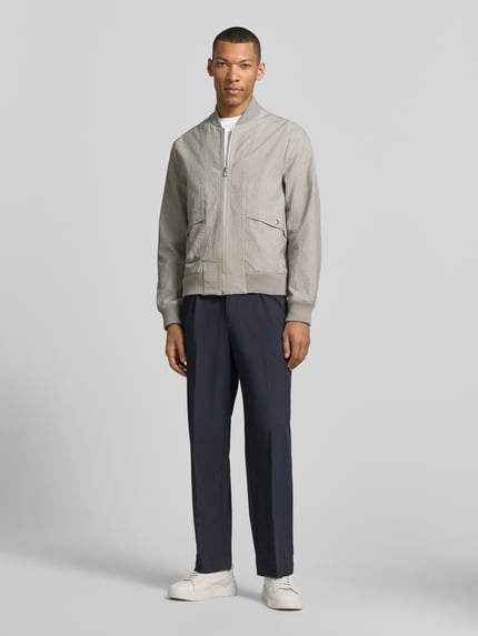 Männermodel trägt Bomberjacke mit Pattentaschen und Reißverschluss von PAUL SMITH, hellgrau, Loose-Fit, Ganzkörperansicht von vorne, Herren, Stehkragen, Druckknopfverschluss, gerippte Abschlüsse, Rückenlänge 65 cm, Schulterbreite 44 cm, Brustweite 53 cm, Ärmellänge 67 cm.