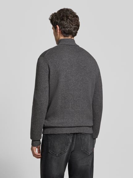 Männermodel trägt Troyer aus Wolle mit Logo-Patch von LACOSTE in Dunkelgrau, Strickstruktur, Regular Fit, Ganzkörperansicht Rückansicht.