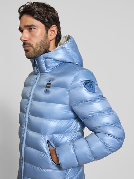 Männermodel trägt Steppjacke mit Zweiwege-Reißverschluss Modell 'ADAMS' von Blauer USA in Hellblau, glänzende Oberfläche, Nahaufnahme Oberkörper. Herren Steppjacke, Regular Fit, Kapuze mit Tunnelzug, Label-Detail am Ärmel, Größenangaben laut Kontext.