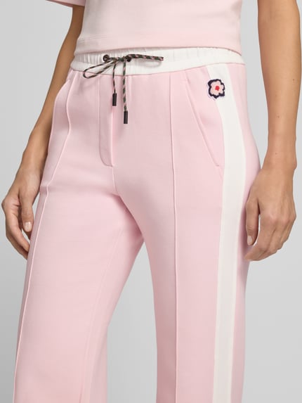 Frauenmodel trägt Straight Fit Hose mit Tunnelzug von Marc Cain in Rosa mit weißem Seitenstreifen, floraler Print am Bund, Nahaufnahme Oberkörper, Damen Hose von Marc Cain, elastischer Bund, Bundweite 36 cm, Innenbeinlänge 68 cm.