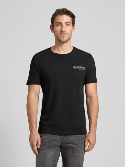 Männermodel trägt Regular Fit T-Shirt aus reiner Baumwolle von Tom Tailor Denim, unifarben schwarz, Rundhals, kurzarm, Label-Schriftzug, Ganzkörperansicht von vorne.
