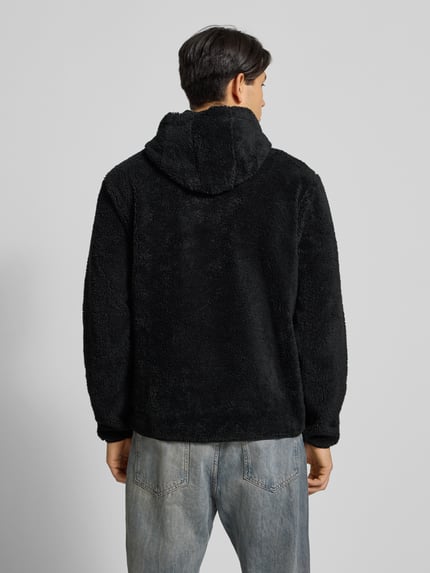 Männermodel draagt Hoodie uit teddybont van CHAMPION in zwart, katoenmix, los model, capuchon, labeldetail en kangoeroezak. Ganzkörperansicht Rückansicht. Ruglengte maat M: 70 cm, mouwlengte maat M: 70 cm.