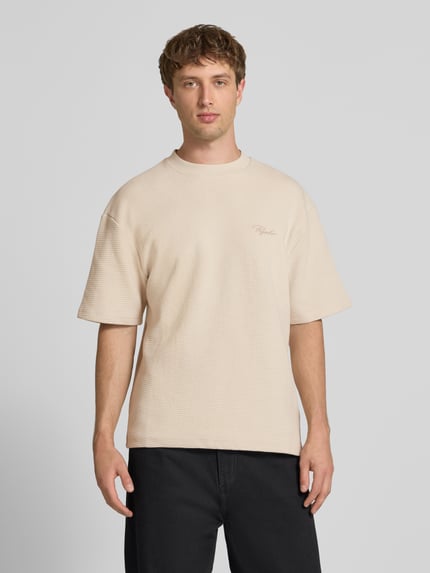 Männermodel trägt Oversized T-Shirt mit Strukturmuster und Label-Stitching von Pegador aus reiner Baumwolle in Beige, Rundhalsausschnitt, Ganzkörperansicht von vorne. Rückenlänge bei Größe M: 70 cm.