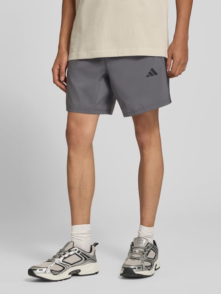 Männermodel trägt graue Regular Fit Sportshorts mit Logo-Print Modell 'WE BAS 3SWV SH' von adidas, Kontext: adidas Training, Nahaufnahme Oberschenkel.