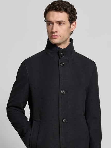 Männermodel trägt unifarbene, matte Daunenjacke Modell 'Fynn' mit Stehkragen von Strellson, strukturierte Optik, Knopfleiste, seitliche Eingrifftaschen, Nahaufnahme Oberkörper.