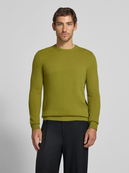 Männermodel trägt Kaschmirpullover mit gerippten Abschlüssen von Christian Berg Men in Olivgrün, glatte Textur, Ganzkörperansicht von vorne. Rückenlänge bei Größe M 72 cm, Ärmellänge 72 cm, gerader Schnitt, Rundhalsausschnitt, reines Kaschmir.