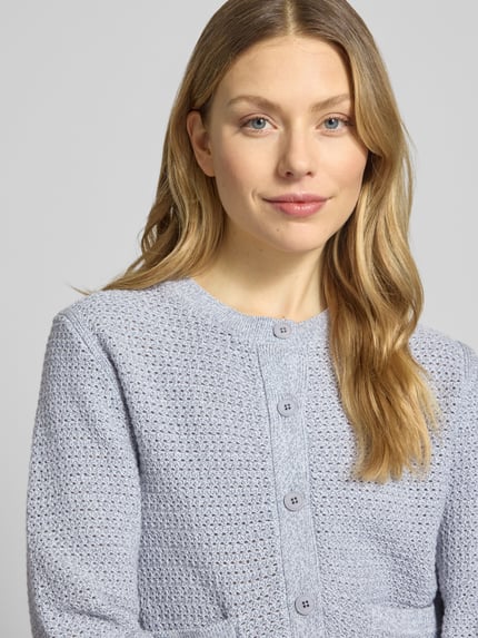 Frauenmodel trägt Regular Fit Strickjacke mit aufgesetzten Taschen Modell 'Biaphy' von Drykorn aus Reine Baumwolle, Knopfleiste, Rundhalsausschnitt, Struktur in Hellgrau, Nahaufnahme Oberkörper.