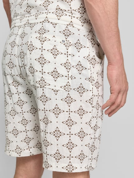 Męski model nosi Relaxed Fit Stoffshorts aus einer Baumwolle od s.Oliver RED LABEL, kremowe i brązowe wzory, tekstura miękka, całkowity widok z tyłu.